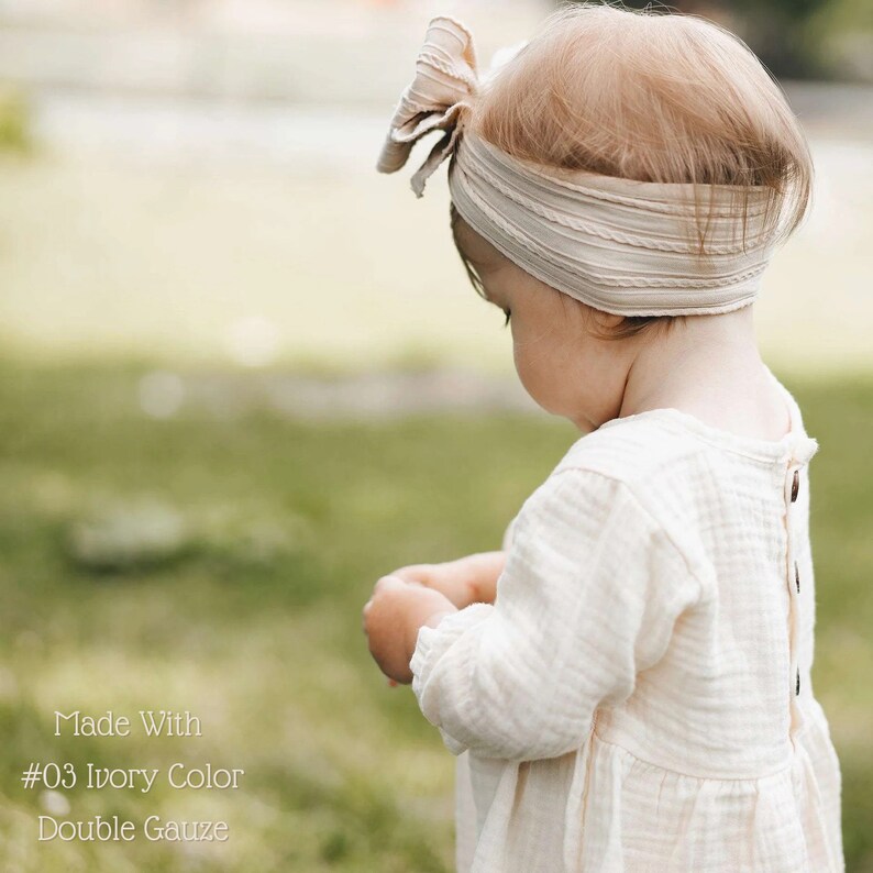 May include: A young child wearing a white dress with a bow headband. The dress is made of double gauze fabric and is ivory in color. The text "Made With #03 Ivory Color Double Gauze" is visible at the bottom of the image.