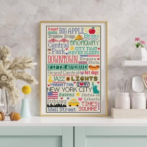 Può includere: Un'opera d'arte a punto croce incorniciata con monumenti e frasi iconiche di New York City, tra cui "Big Apple", "Broadway" e "Statua della Libertà". L'opera, in una cornice dorata, include un taxi giallo e un hot dog.