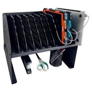 May include: A black metal charging station with seven numbered slots for tablets and laptops. The station holds various devices, including an orange and black tablet, a blue and black tablet, and a silver laptop. A stapler, scissors, and a pen holder are also visible.