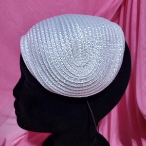 May include: A pale grey woven hat with a rounded crown. The hat is displayed on a black mannequin head against a pink backdrop. The hat's texture is visible, with a repeating pattern of horizontal lines.