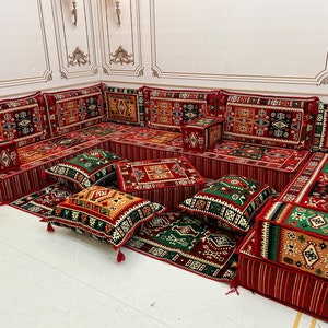 May include: A traditional red and green patterned floor seating set with multiple cushions and pillows. The set is arranged in a U-shape and features intricate geometric designs.