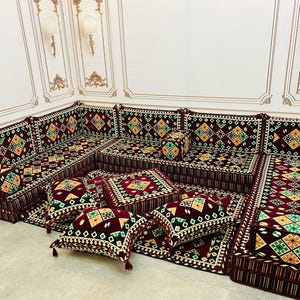 Puede incluir: Un arreglo tradicional de asientos de piso del Medio Oriente, conocido como majlis, con cojines estampados en rojo, verde y dorado y una alfombra a juego. Los cojines están dispuestos en forma de U, con un pequeño cojín cuadrado en el centro.