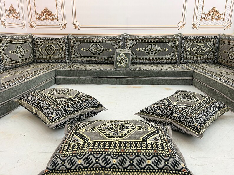 May include: A gray and black patterned floor cushion set with a traditional Moroccan design. The set includes a large L-shaped sofa, four square cushions, and a small square ottoman.