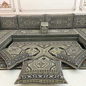 May include: A gray and black patterned floor cushion with a geometric design. The cushion is part of a larger set of cushions and a sofa, all with the same pattern.
