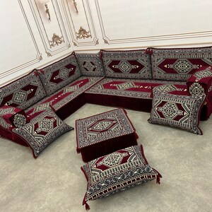 May include: A burgundy and gold patterned floor seating set with a square ottoman and multiple cushions. The set is arranged in a traditional Moroccan style.