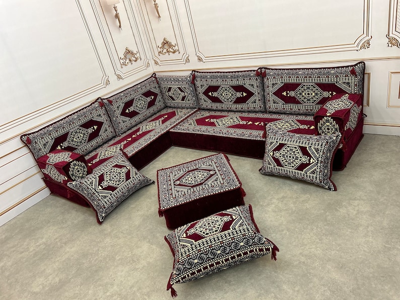 May include: A burgundy and gold patterned floor seating set with a square ottoman and multiple cushions. The set is arranged in a traditional Moroccan style.