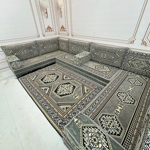 May include: A gray and black patterned floor cushion set with a matching rug. The cushions are arranged in a U-shape and are perfect for lounging. The rug has a geometric design and is made of a soft, plush material.