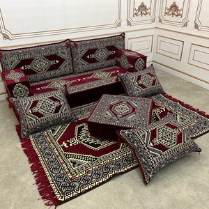 May include: A burgundy and black patterned floor cushion set with a matching rug. The set includes a large sofa cushion, several smaller cushions, and a square ottoman.