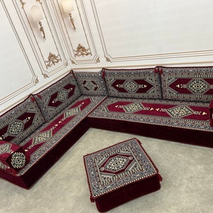 May include: A burgundy and gold patterned floor seating set with a matching ottoman. The set is made of plush fabric and features intricate geometric designs.