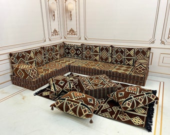 May include: A brown and beige patterned floor seating set with a corner sofa, four square cushions, and a rectangular rug. The sofa and cushions have a geometric design with black accents.