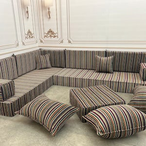 Puede incluir: Un sofá seccional con tapicería a rayas en tonos marrones, beige y negros. El sofá tiene varios cojines y un otomano a juego.