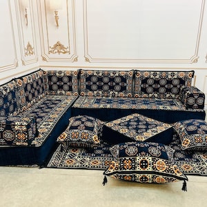 May include: A black and gold patterned floor cushion set with a couch-like configuration. The set includes a large couch, two smaller cushions, and a rug. The cushions are all covered in a black fabric with a gold geometric pattern.