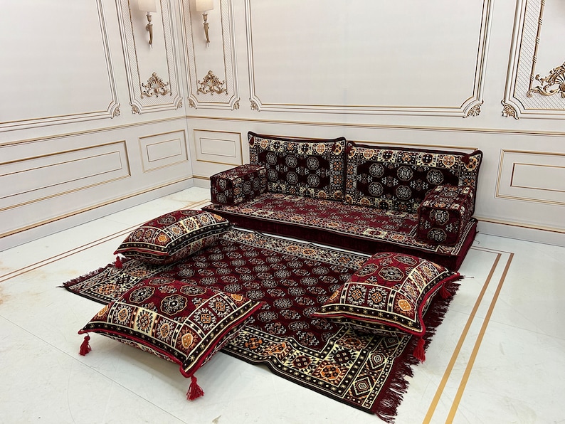 K&ouml;nnte beinhalten: Ein rotes und goldenes Bodenkissen-Set mit einem gro&szlig;en Sofa und vier kleineren Kissen. Die Kissen sind alle aus einem weichen, pl&uuml;schigen Stoff gefertigt und haben komplizierte Muster.