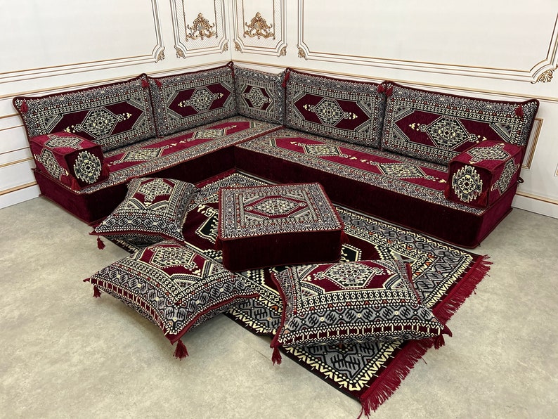 May include: A burgundy and cream colored traditional Moroccan floor seating set with a square ottoman and multiple cushions. The set features intricate geometric patterns and tassels.