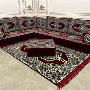 May include: A burgundy red sectional sofa with intricate patterned cushions and a matching burgundy red rug with a geometric pattern. The sofa is set up in a corner and includes a small square ottoman.