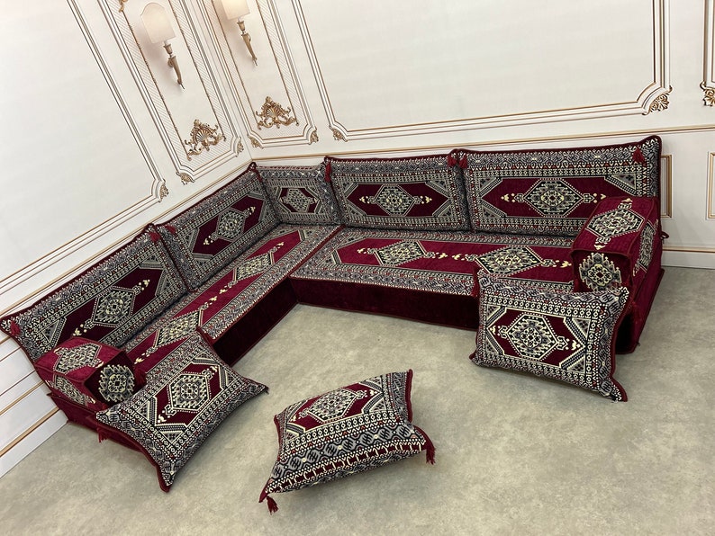 May include: A burgundy and cream colored traditional Moroccan floor seating set with intricate geometric patterns. The set includes a large L-shaped sofa with multiple cushions and several smaller throw pillows.