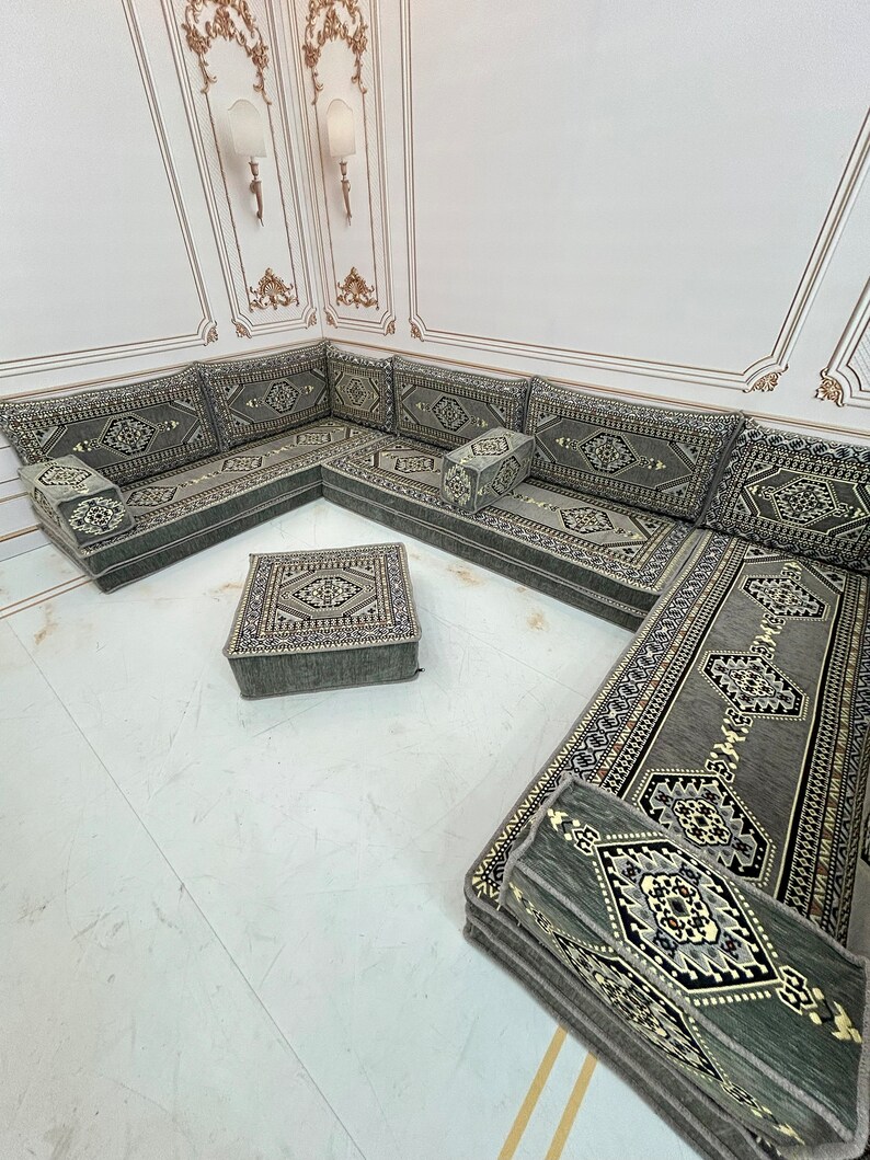 May include: A traditional Moroccan floor seating set with a green and gold patterned fabric. The set includes a large L-shaped sofa, a square ottoman, and several smaller cushions.