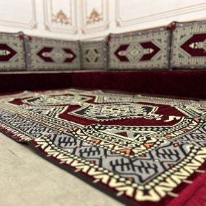 May include: A red and black patterned rug with a geometric design. The rug is placed on top of a burgundy couch with matching patterned cushions.