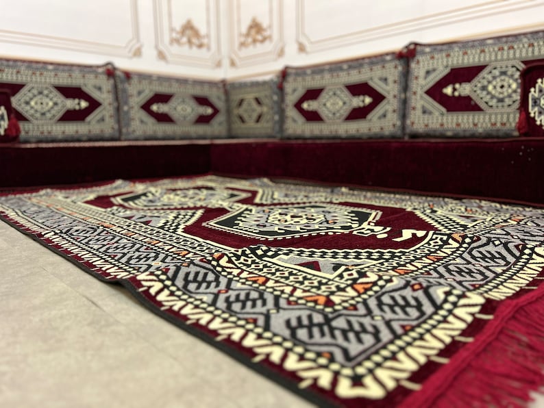 May include: A red and black patterned rug with a geometric design. The rug is placed on top of a burgundy couch with matching patterned cushions.