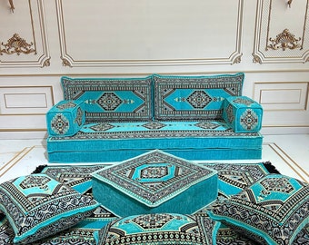 May include: A turquoise and black patterned floor cushion set with a matching ottoman. The set includes a large floor cushion, two smaller floor cushions, and a square ottoman. The cushions and ottoman are all covered in a soft, plush fabric with a geometric pattern.