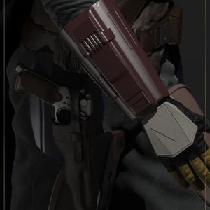May include: A close-up of a character from the Mandalorian TV series, wearing a dark grey outfit with a brown leather belt and a red and grey forearm armor piece. The character is holding a blaster rifle in their left hand.