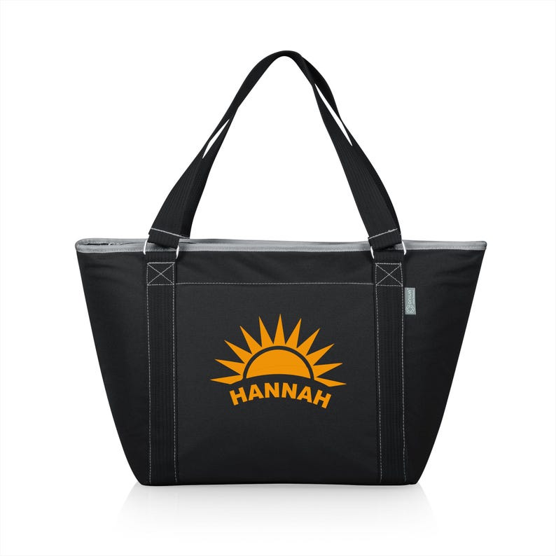 Puede incluir: Bolsa de transporte aislada negra con cierre de cremallera y dos asas superiores. La bolsa presenta un gr&aacute;fico de sol amarillo con el nombre "HANNAH" impreso debajo.