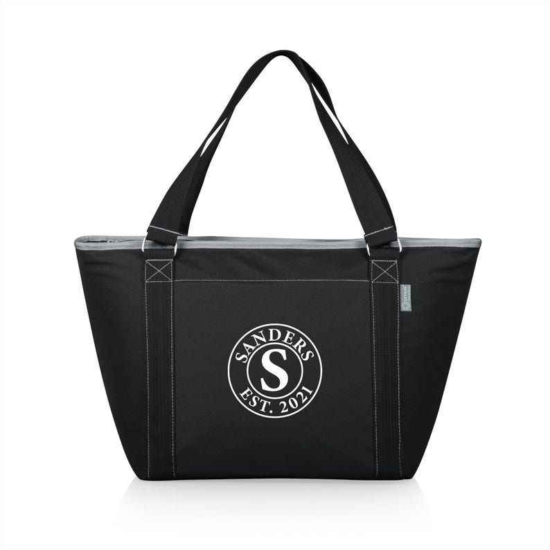Puede incluir: Bolsa de transporte aislada negra con una cremallera blanca y dos asas negras. La bolsa tiene un logotipo circular blanco con el texto "SANDERS EST. 2021" y una letra "S" blanca en el centro.