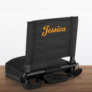 May include: Black stadium seat with a backrest. The word "Jessica" is printed in orange script on the back. Includes a black shoulder strap and a black base with the word "OMUA" printed on it.
