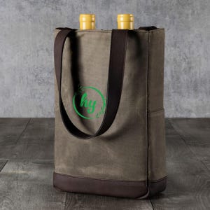 May include: A brown canvas wine tote bag with two brown leather straps and a brown leather bottom. The bag has a green embroidered logo that says "hy" with a leaf design.