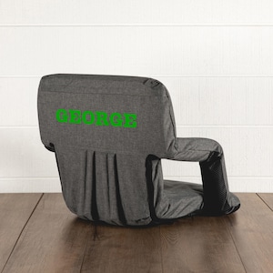 May include: A gray floor chair with armrests and a backrest. The word "GEORGE" is printed in green on the backrest. The chair is designed for floor use and has a pleated design on the back.