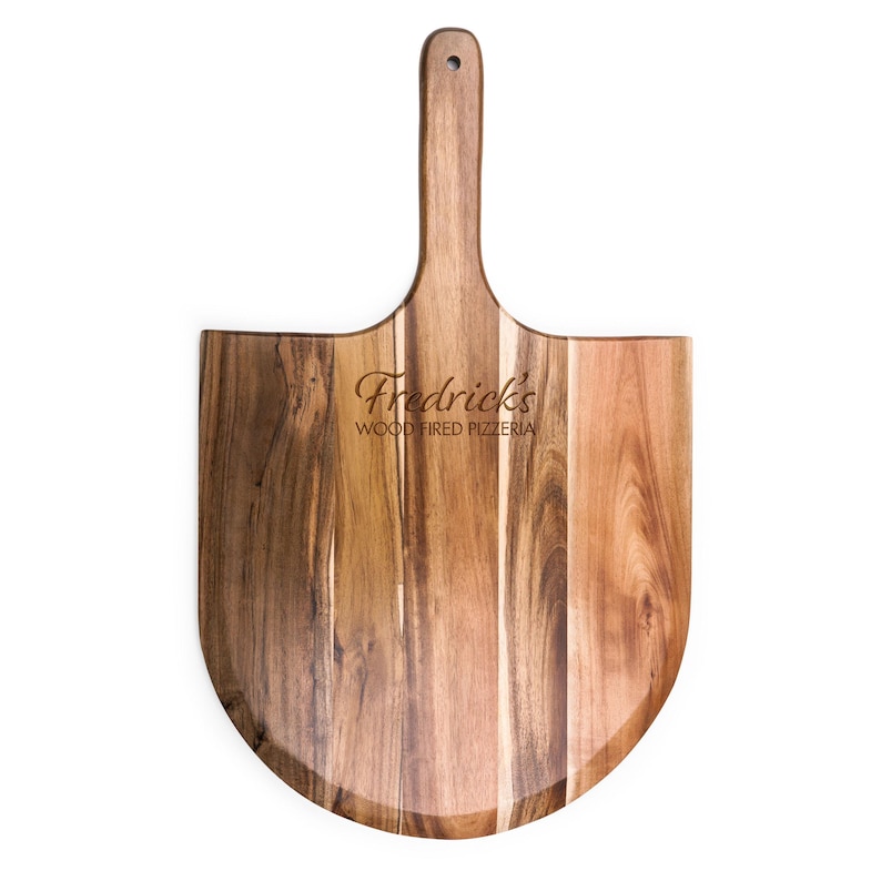 May include: A wooden pizza peel with a long handle and a rounded blade, featuring a natural wood grain pattern in shades of brown. The text "Fredrick's WOOD FIRED PIZZERIA" is engraved in the center of the blade, and a small hole is at the top.