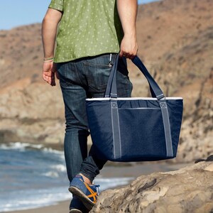 Puede incluir: Una persona llevando una bolsa de transporte aislada azul y blanca con cierre de cremallera. La bolsa tiene dos asas grandes y un forro blanco.