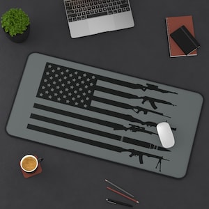 May include: A gray and black mouse pad with a silhouette of an American flag and various firearms. The flag has 13 stripes and 50 stars.