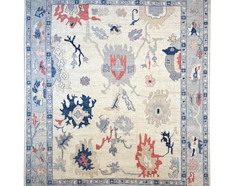 May include: A beige rug with a blue and red floral pattern. The rug has a border with a repeating pattern of flowers and leaves.