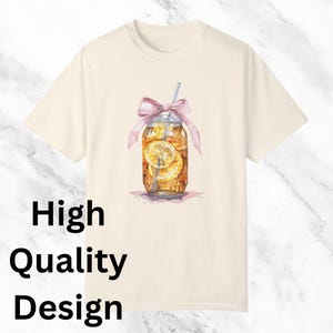 Peut inclure: Un t-shirt cr&egrave;me avec une illustration aquarelle d'un bocal en verre rempli de th&eacute; glac&eacute; et de tranches de citron. Le bocal est orn&eacute; d'un ruban rose et d'une paille qui d&eacute;passe. Le texte "High Quality Design" est imprim&eacute; dans le coin inf&eacute;rieur gauche du t-shirt.