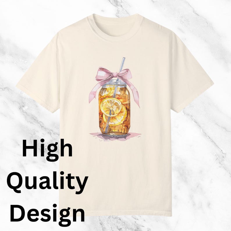 Peut inclure: Un t-shirt cr&egrave;me avec une illustration aquarelle d'un bocal en verre rempli de th&eacute; glac&eacute; et de tranches de citron. Le bocal est orn&eacute; d'un ruban rose et d'une paille qui d&eacute;passe. Le texte "High Quality Design" est imprim&eacute; dans le coin inf&eacute;rieur gauche du t-shirt.