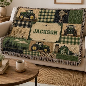 May include: A woven throw blanket with a patchwork design featuring green tractors, plaid patterns, a windmill, and a barn. The blanket has a beige background and the name "JACKSON" is displayed in a central label. The blanket has a fringed edge.