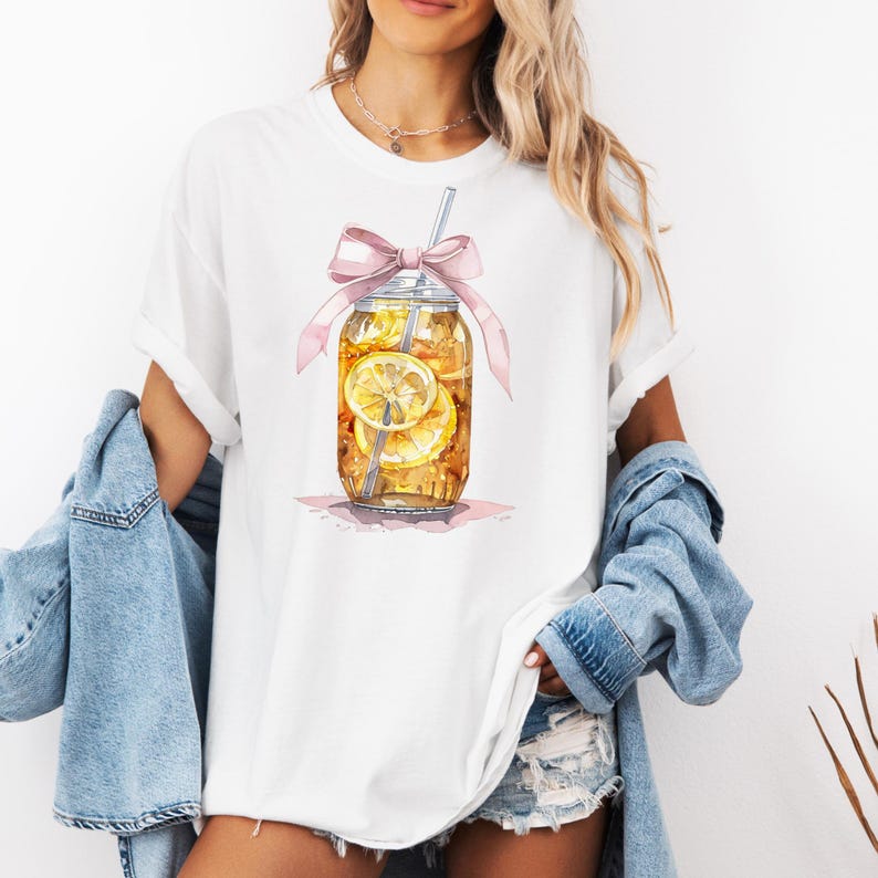 Peut inclure: T-shirt blanc avec un motif repr&eacute;sentant un bocal en verre rempli de th&eacute; glac&eacute; et de tranches de citron, surmont&eacute; d'un n&oelig;ud rose et d'une paille.