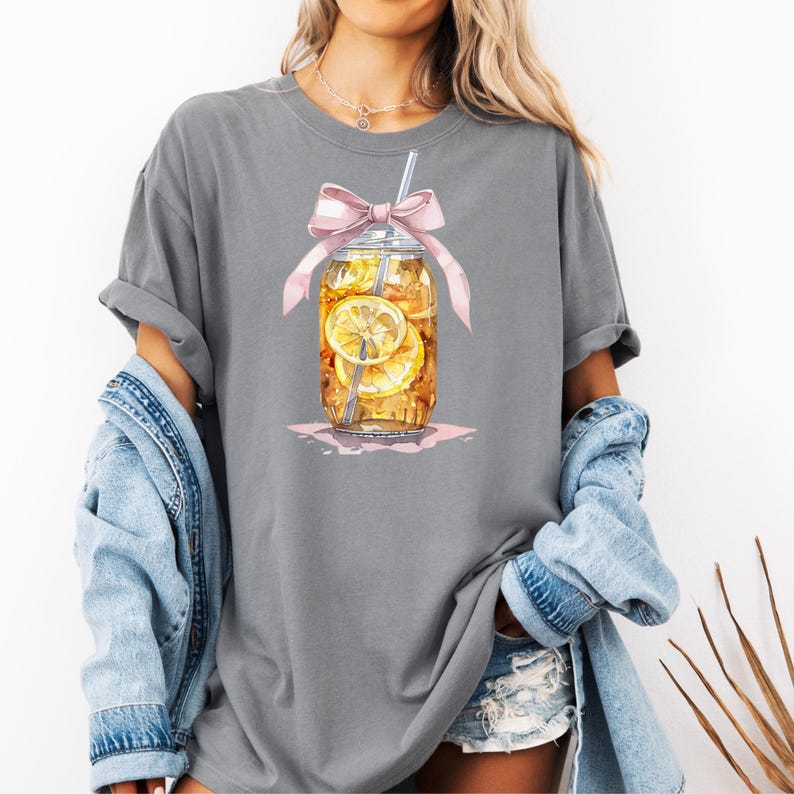 Peut inclure: Un t-shirt gris avec un motif repr&eacute;sentant un bocal en verre rempli de th&eacute; glac&eacute; et de tranches de citron. Le bocal est orn&eacute; d'un ruban rose et d'une paille.