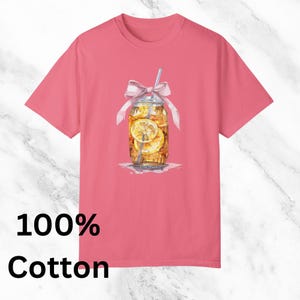 Peut inclure: Un t-shirt rose avec un motif repr&eacute;sentant un bocal en verre rempli de th&eacute; glac&eacute; et de tranches de citron. Le bocal est orn&eacute; d'un ruban rose et d'une paille qui d&eacute;passe. Le texte "100% Coton" est imprim&eacute; sous l'image.