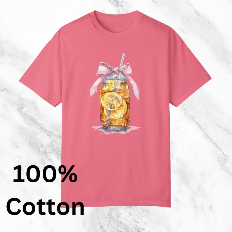 Peut inclure: Un t-shirt rose avec un motif repr&eacute;sentant un bocal en verre rempli de th&eacute; glac&eacute; et de tranches de citron. Le bocal est orn&eacute; d'un ruban rose et d'une paille qui d&eacute;passe. Le texte "100% Coton" est imprim&eacute; sous l'image.