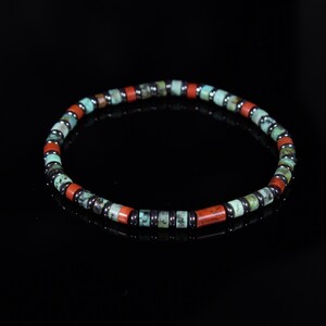 May include: A beaded bracelet featuring a mix of red, turquoise, and dark gray beads. The bracelet is made of small, cylindrical beads and is strung together on an elastic band. The beads are arranged in a repeating pattern.