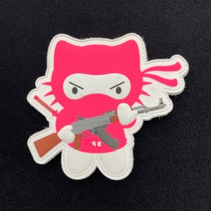 May include: Pink Hello Kitty character wearing a white ninja mask and holding a brown and silver AK-47 rifle. The character is wearing a pink headband and has a white outline.
