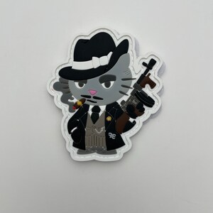 May include: A gray cat wearing a black fedora, a white vest, and a black suit, holding a brown and black machine gun and smoking a cigar. The cat has a pink nose and a mustache. The image is a patch with a white background and a white stitched border.