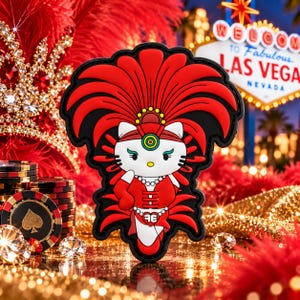 May include: A rubberized patch featuring a white cat character wearing a red showgirl costume with a large red feather headdress, a pearl necklace, and a belt with the letters AE, set against a black background with a thick border.