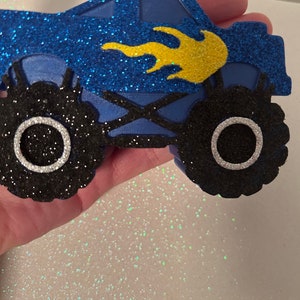 Pu&ograve; includere: Monster truck blu e nero con glitter e fiamme gialle. Il camion ha grandi ruote nere con cerchi argentati.