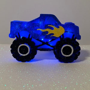 Pu&ograve; includere: Un topper per torta a forma di monster truck blu e oro con glitter. Il camion ha un design a fiamma sul lato ed &egrave; illuminato da luci blu.