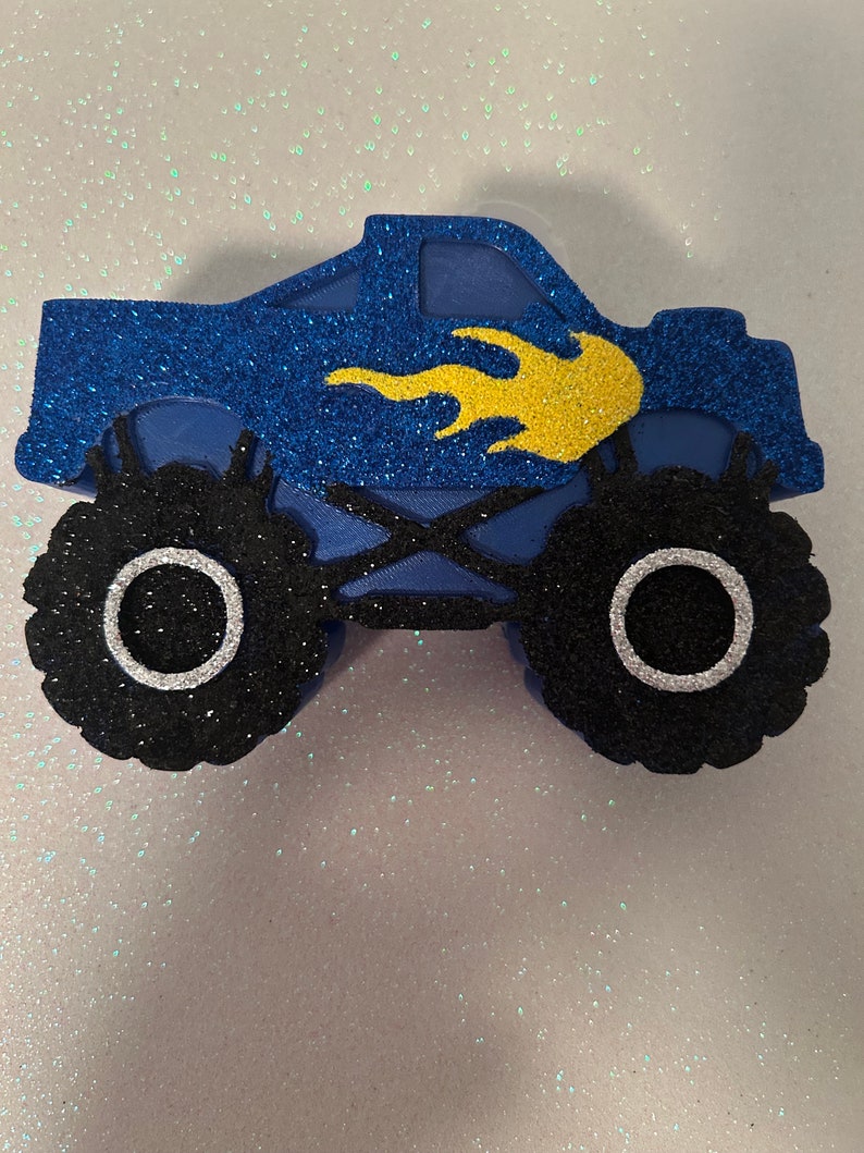 Pu&ograve; includere: Camion monster blu con fiamme gialle, pneumatici neri con cerchi bianchi e finitura glitter.