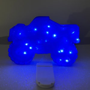 Pu&ograve; includere: Una luce notturna a forma di monster truck blu con luci LED bianche. La luce &egrave; accesa e la luce blu illumina il camion.