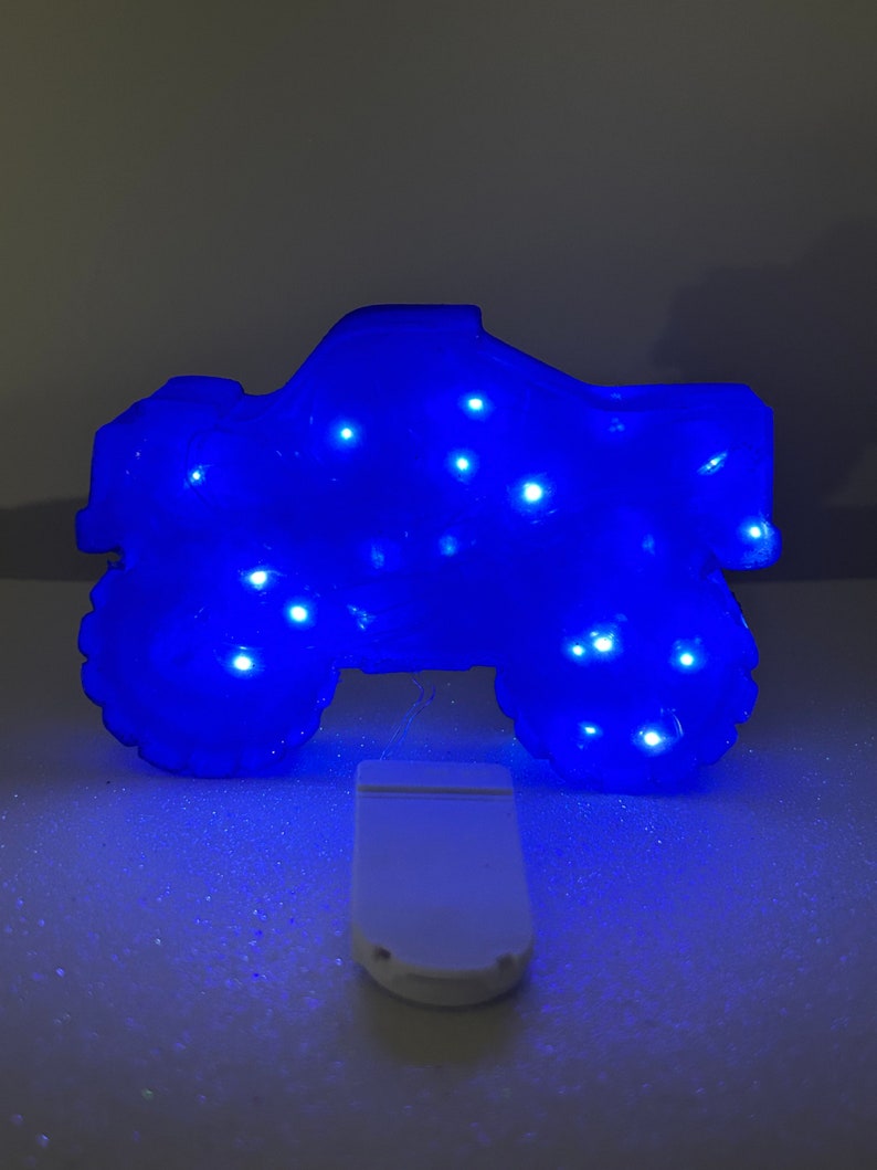 Pu&ograve; includere: Una luce notturna a forma di monster truck blu con luci LED bianche. La luce &egrave; accesa e la luce blu illumina il camion.